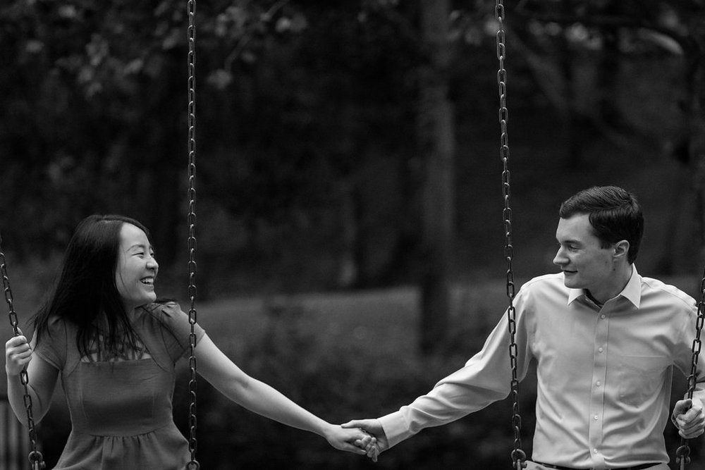 Black and white photo of couple swinging in Freedom Park in Charlotte, North Carolina. Engagement Photography by Party of Two Photography.