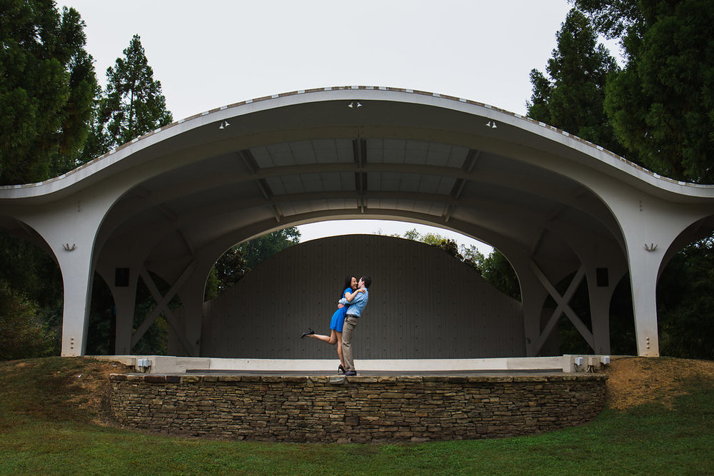 Fun engagement photo of guy lifting girl in an amphitheater in Freedom Park in Charlotte, North Carolina. Engagement Photography by Party of Two Photography.