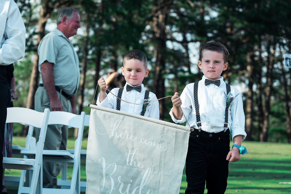 Two children bring wedding sign down aislein Pilot Knob Country Club. Wedding Photography by Party of Two Photography.