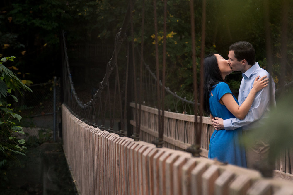 Sweet engagement photo of couple kissing on bridge in Freedom Park in Charlotte, North Carolina. Engagement Photography by Party of Two Photography.