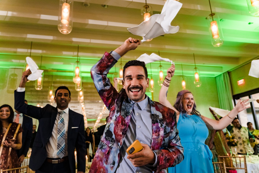 Guests introduce bride and groom with waving napkins for colorful summer Indian Wedding
