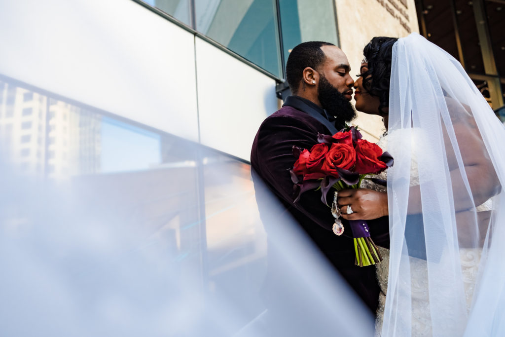 Cute photo of bride and groom with veil and flowers outside of the Mint Museum during their wedding day in Uptown Charlotte