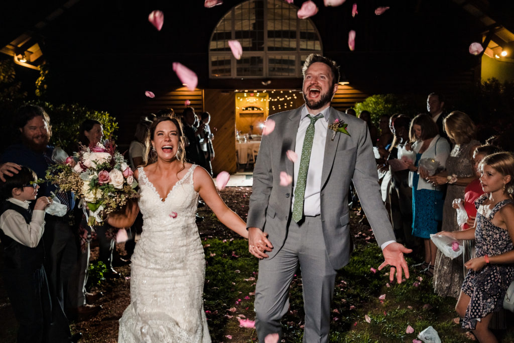 Pure joy on Megan and Mickey's face as they exit the barn of Alexander Homestead while wedding guests throw pink flower petals at them.
