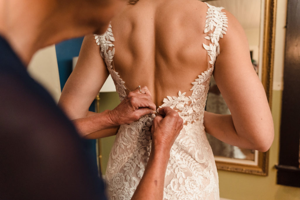Bride putting on wedding dress with mother helping button up