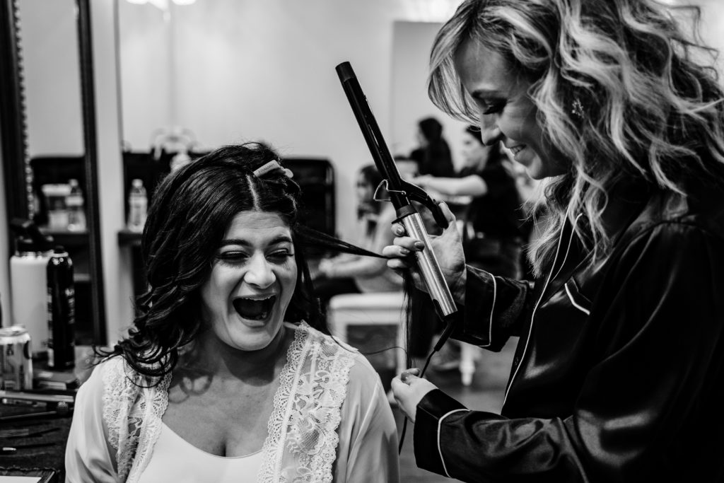 Bride and maid of honor sharing funny moment together while getting hair done