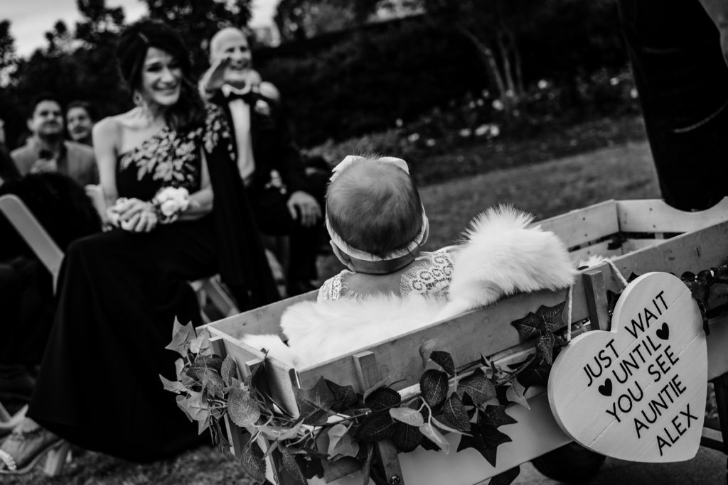 Baby in wagon with a sign coming down the wedding aisle at Sweet Magnolia Estate