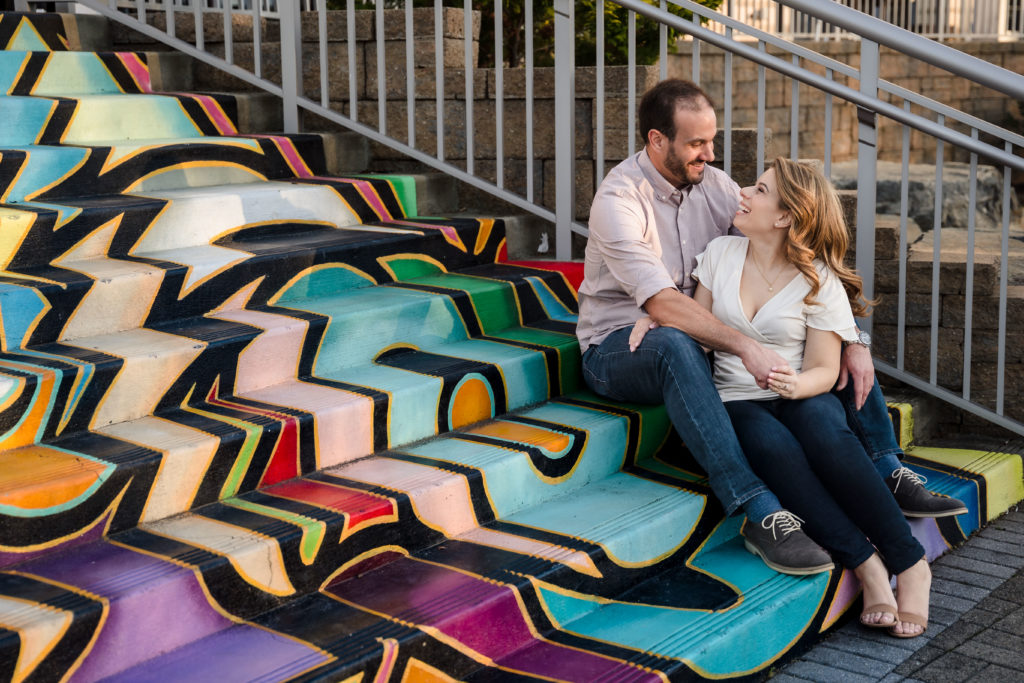 Couple seated on steps with multicolored mural during Colorful Charlotte engagement session