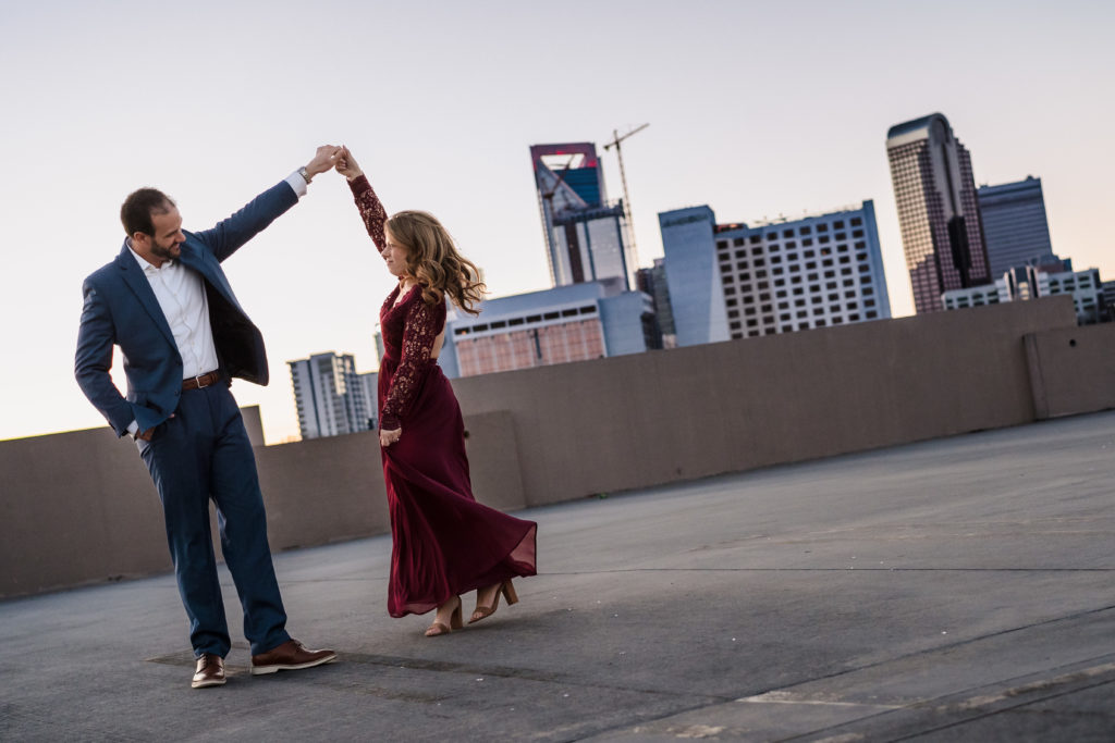 Couple dancing in front of colorful Charlotte skyline for engagement session