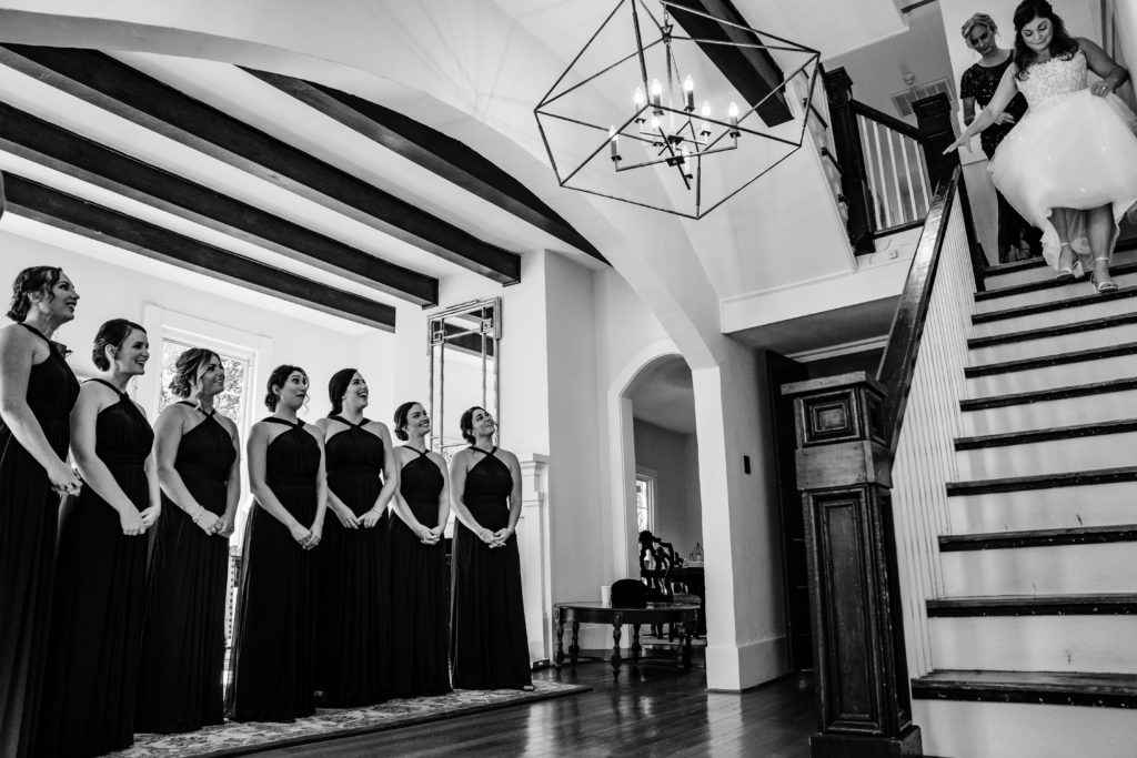 Bride revealing her wedding dress to bridesmaids on stairs of Venue at Langtree