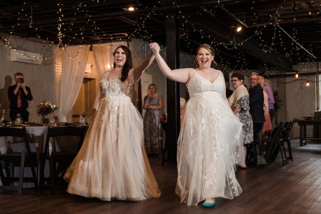 Two brides entering industrial wedding reception