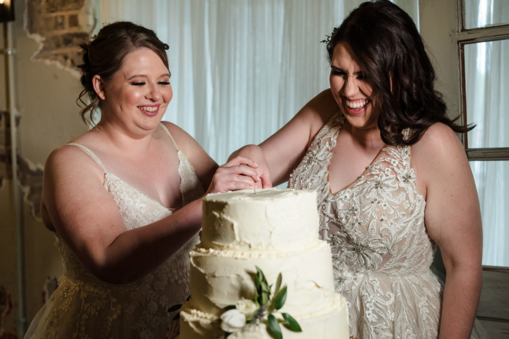 Two brides cut cake at industrial wedding