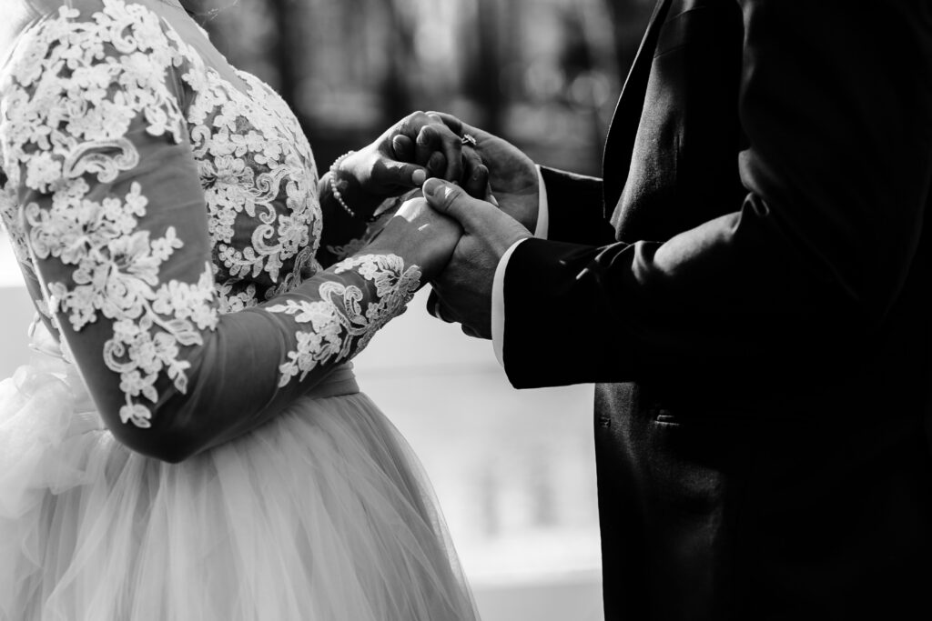 Black and white detail photography of Bride with highly detailed lace dress holding hands with groom.