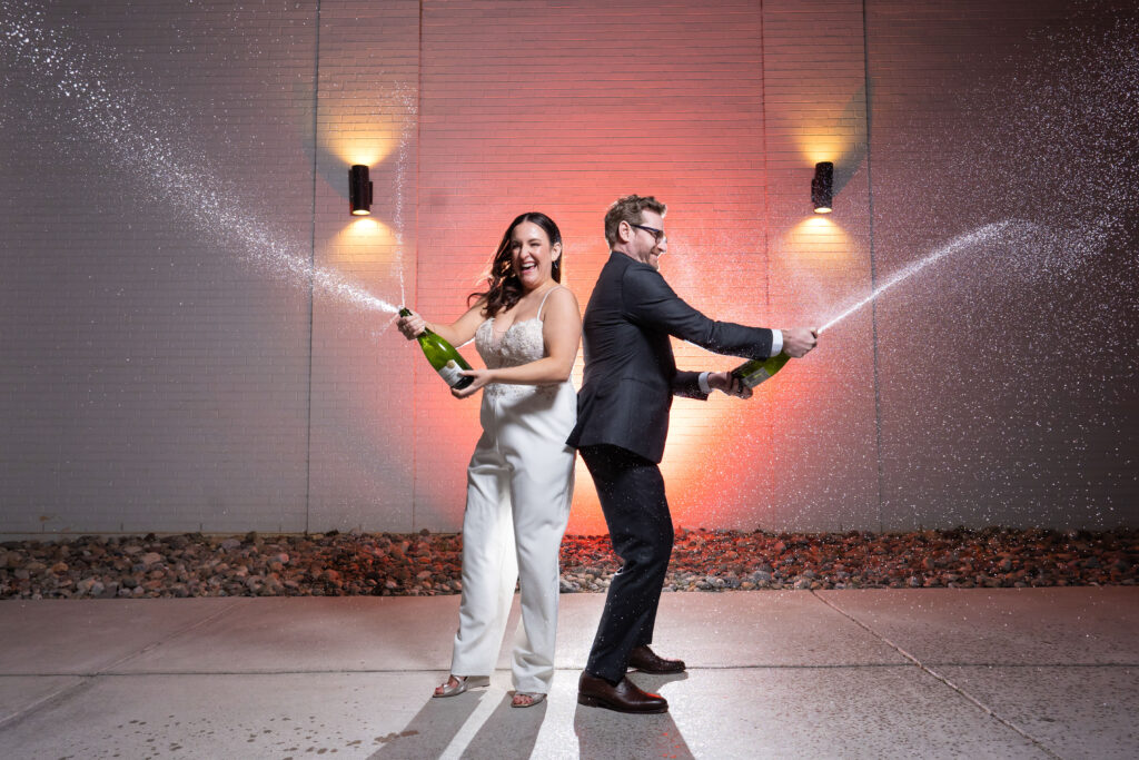 Wedding couple celebrating New Years Eve by spraying champagne outside and laughing